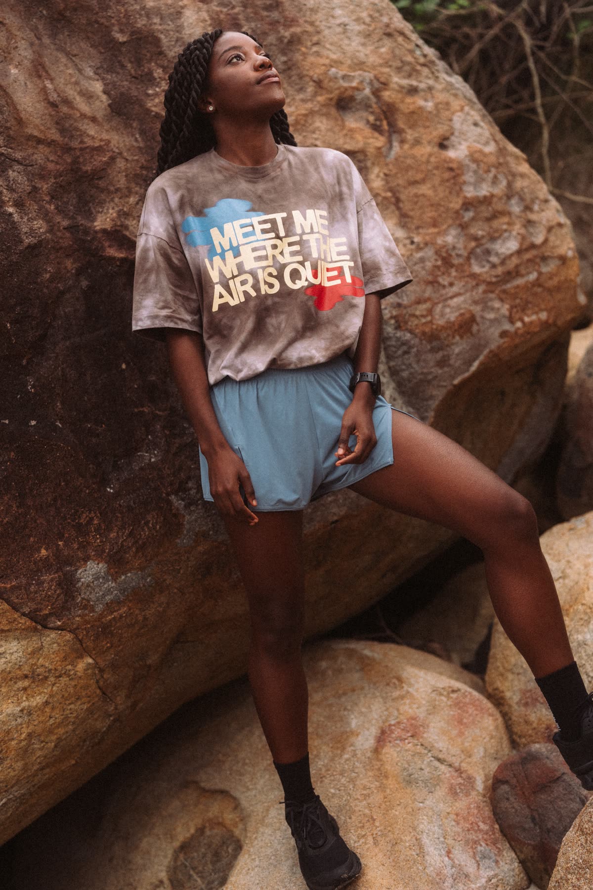 Corredora encostada na pedra com a camiseta “Meet me where the air is quiet” e shorts azul
