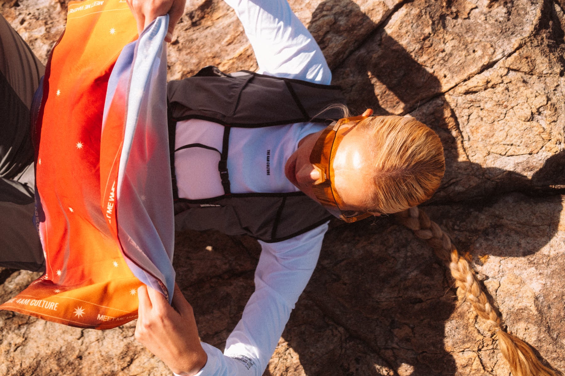 Vista de cima: corredora na pedra abrindo a bandana laranja