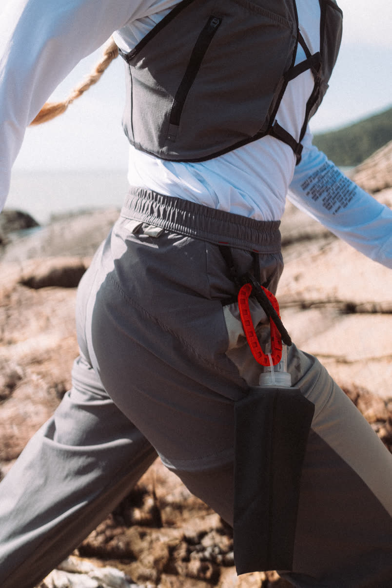 Detalhe da calça com mosquetão vermelho e garrafa na lateral